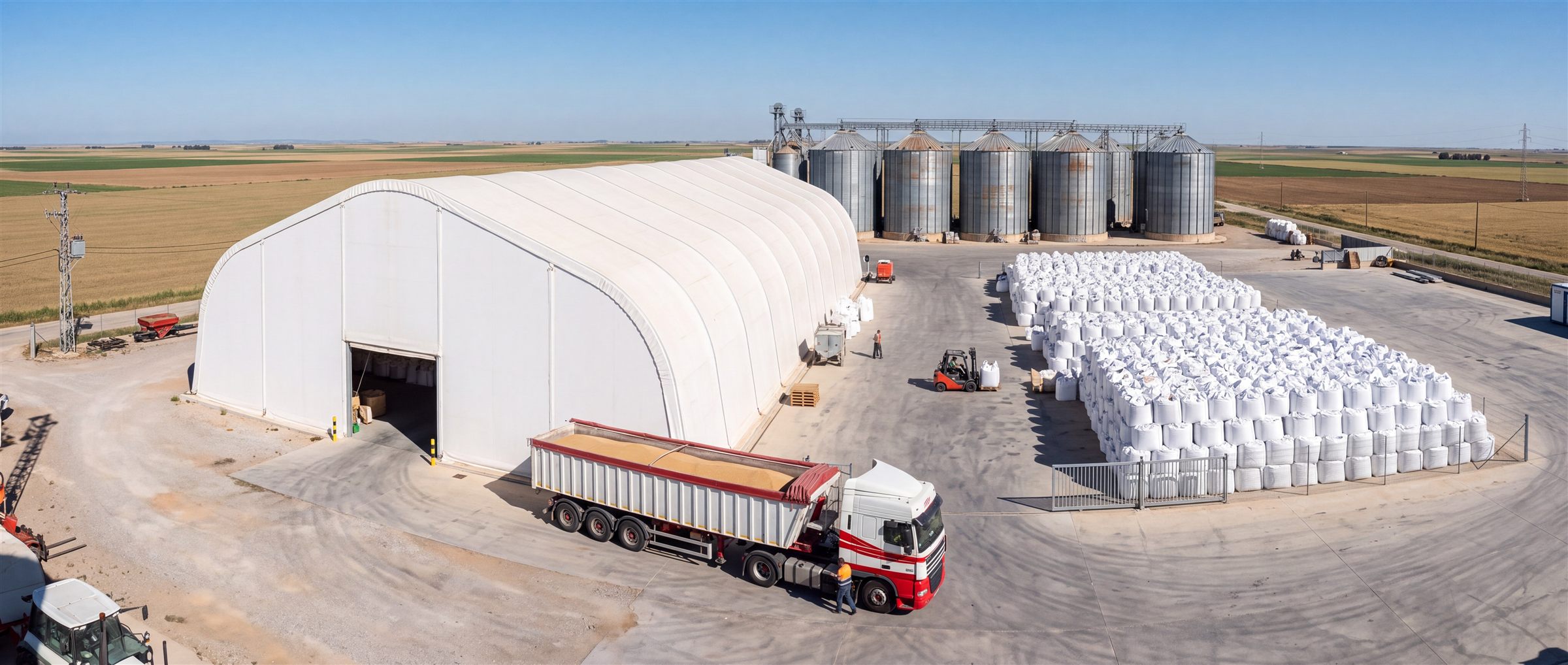 Planta agroindustrial con galpón de lona tensada y silos al fondo.