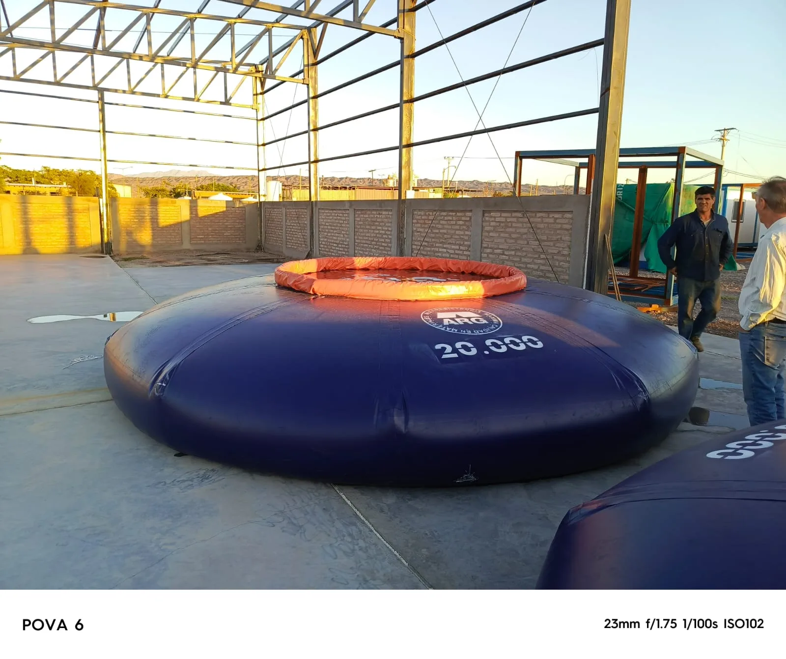 Flexitank autosoportado de gran capacidad lleno de agua en una explanada de operación minera, montañas áridas de fondo, fotografía industrial realista panorámica