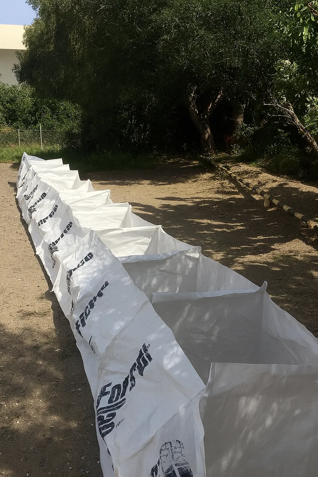 Barrera de contención ForceBag de celdas desplegables rellenas de tierra formando un dique a lo largo de un cauce, maquinaria de obra al fondo, fotografía industrial realista panorámica